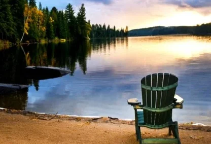 Chair on the edge of the lake as the trees reflect off of the water